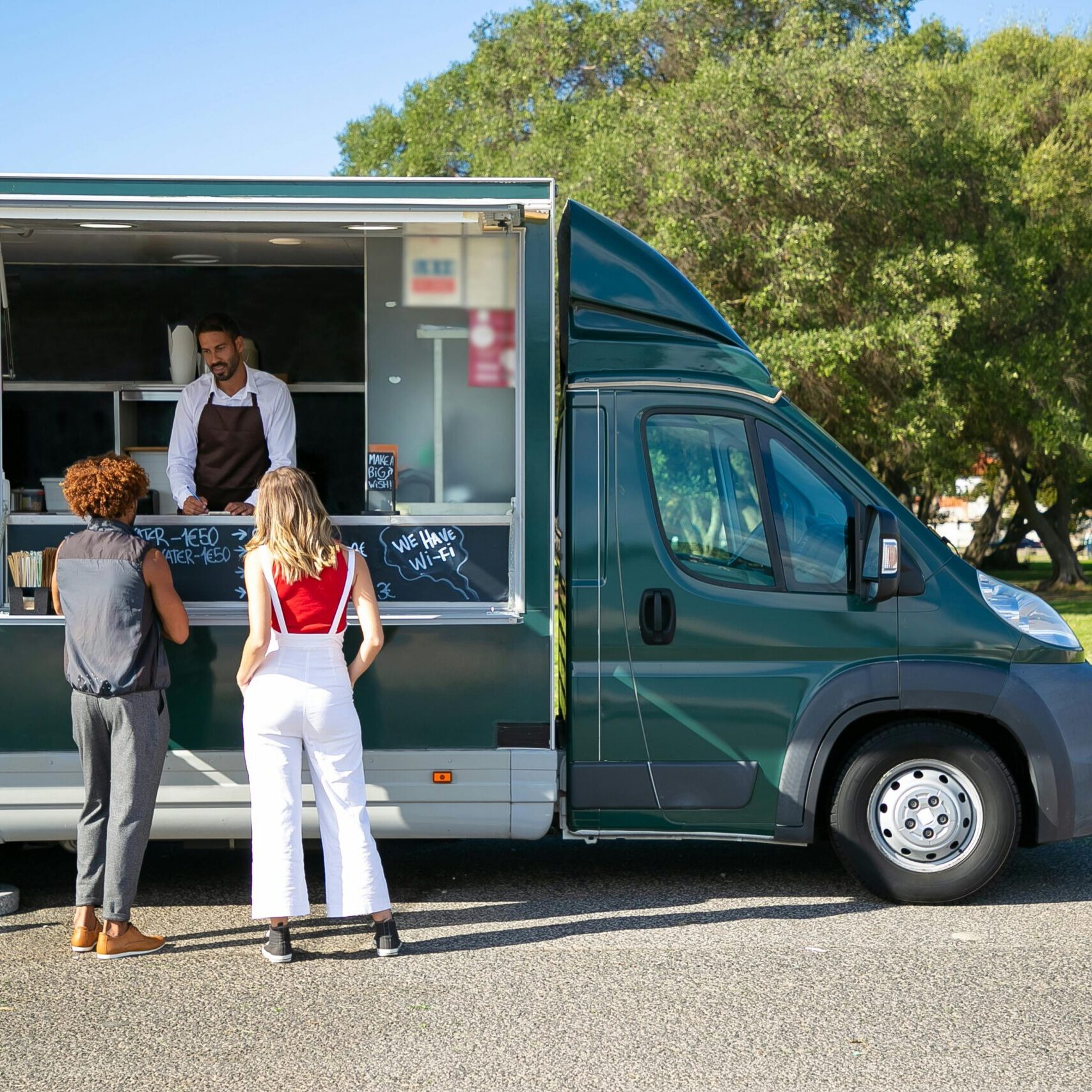 Customers ordering at a food truck parked in a sunny park, showcasing mobile dining.